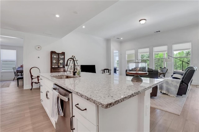 kitchen with light stone countertops, a sink, open floor plan, light wood-type flooring, and stainless steel dishwasher