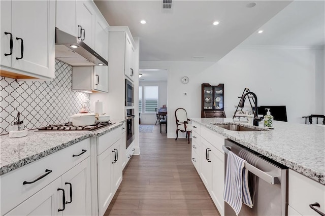kitchen featuring decorative backsplash, appliances with stainless steel finishes, a sink, light stone counters, and under cabinet range hood
