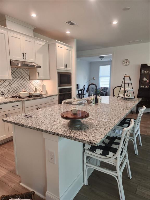 kitchen featuring visible vents, wood finished floors, oven, a kitchen bar, and white cabinetry