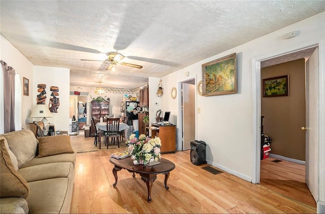 living room featuring light hardwood / wood-style flooring, ceiling fan, and a textured ceiling