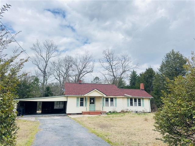 ranch-style home featuring aphalt driveway, an attached carport, a chimney, and a front lawn