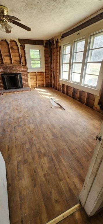 unfurnished living room featuring a textured ceiling, wood-type flooring, a wealth of natural light, and a brick fireplace