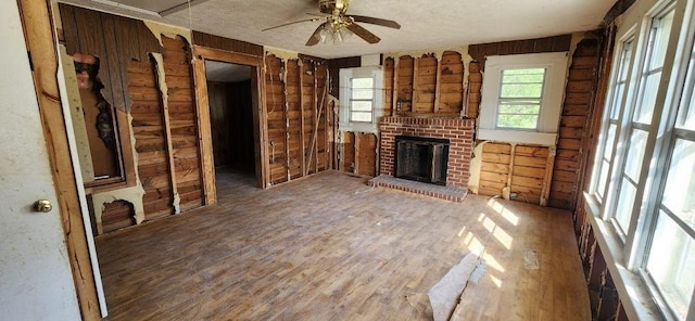 unfurnished living room with a textured ceiling, ceiling fan, a fireplace, and wood finished floors