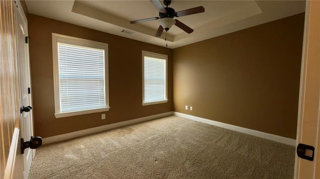 unfurnished room with carpet floors, a raised ceiling, visible vents, a ceiling fan, and baseboards