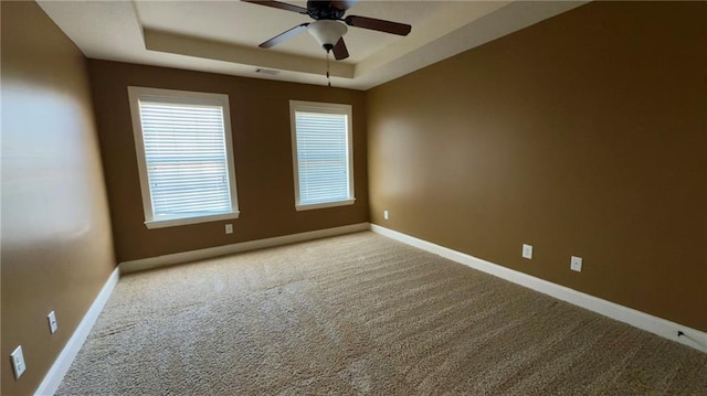 unfurnished room with a tray ceiling, visible vents, a ceiling fan, carpet flooring, and baseboards