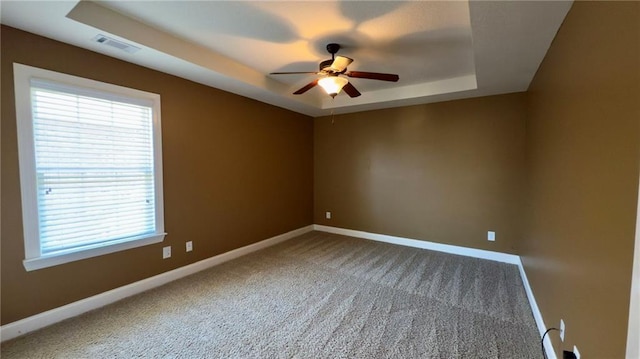 unfurnished room with a tray ceiling, visible vents, and baseboards