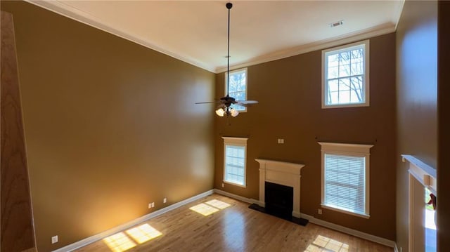 unfurnished living room with a fireplace with raised hearth, visible vents, baseboards, ornamental molding, and light wood finished floors