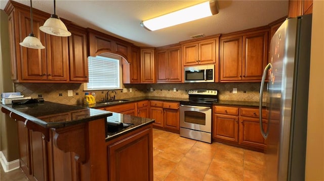 kitchen featuring dark countertops, hanging light fixtures, appliances with stainless steel finishes, a sink, and a peninsula