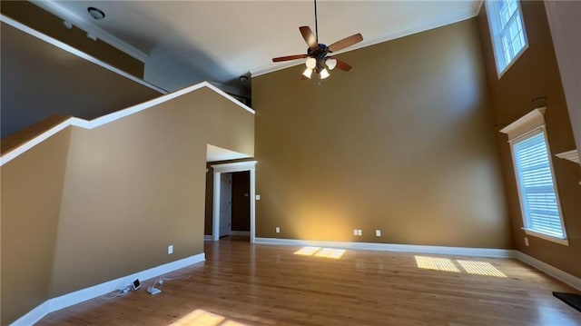 unfurnished living room with baseboards, ceiling fan, a high ceiling, and light wood-style floors