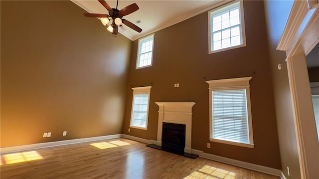 unfurnished living room featuring light wood finished floors, baseboards, a fireplace with raised hearth, and ornamental molding