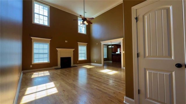 unfurnished living room with a fireplace with raised hearth, ceiling fan, light wood-style flooring, baseboards, and crown molding