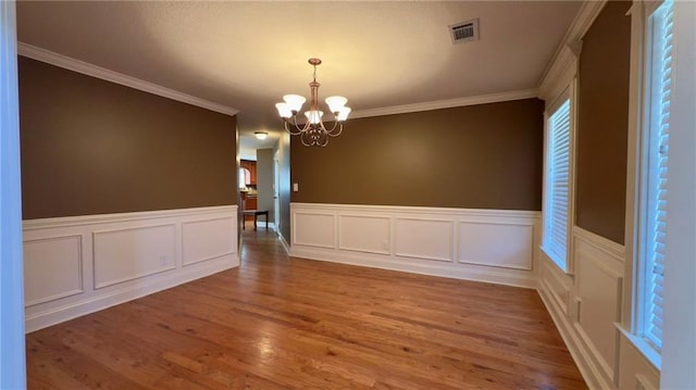 spare room with a chandelier, visible vents, ornamental molding, and wood finished floors