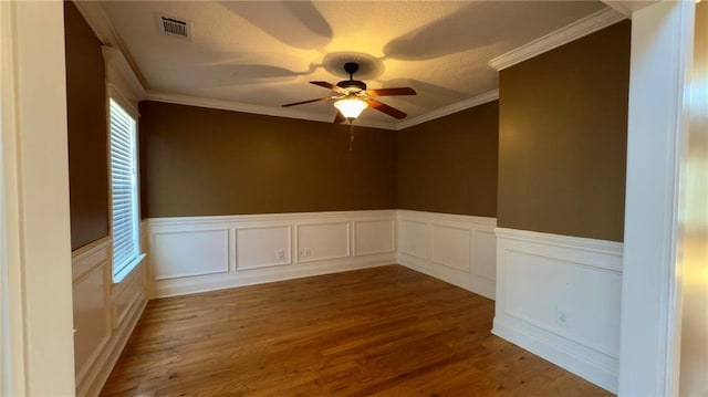 empty room with crown molding, wood finished floors, visible vents, and a ceiling fan