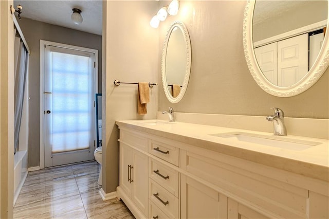 full bath with toilet, double vanity, and a sink