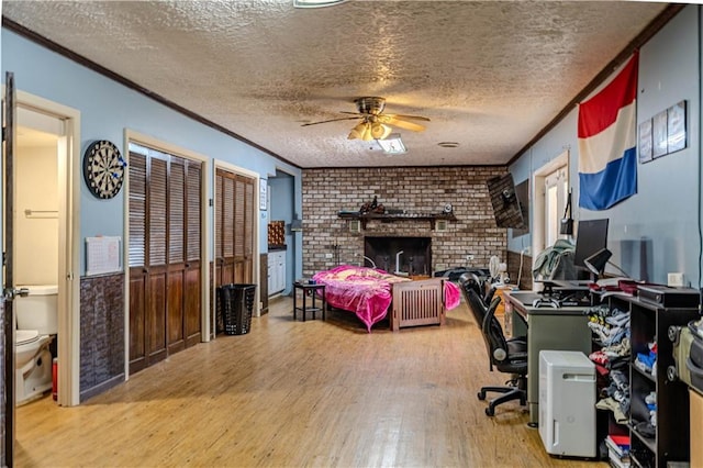 bedroom with a textured ceiling, crown molding, a fireplace, and wood finished floors