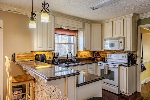 kitchen featuring white appliances, dark wood-type flooring, a peninsula, pendant lighting, and a sink