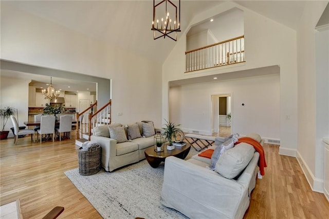 living area featuring stairway, visible vents, light wood finished floors, high vaulted ceiling, and a chandelier