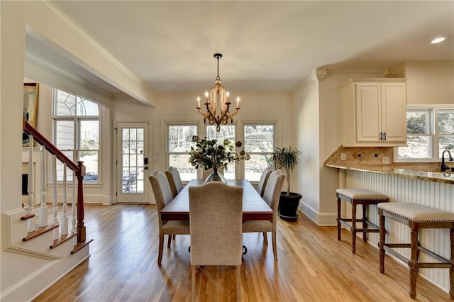 dining space with light wood finished floors, a notable chandelier, crown molding, and baseboards