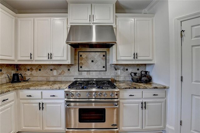 kitchen featuring stainless steel stove, white cabinets, tasteful backsplash, and under cabinet range hood