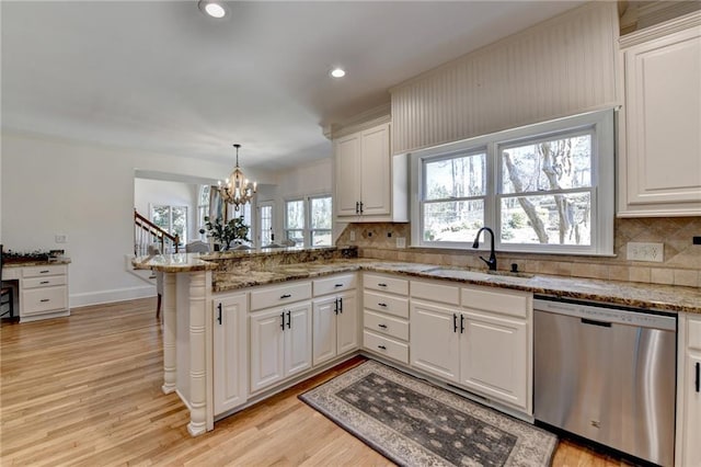 kitchen featuring a peninsula, a sink, white cabinets, dishwasher, and light wood-type flooring