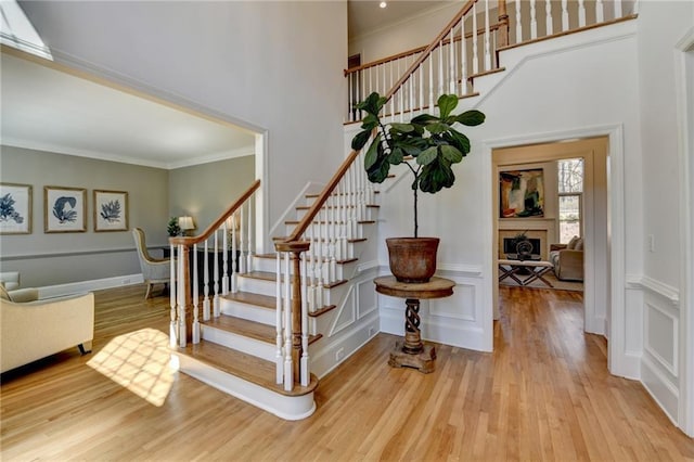 stairway featuring a decorative wall, ornamental molding, a fireplace, and wood finished floors