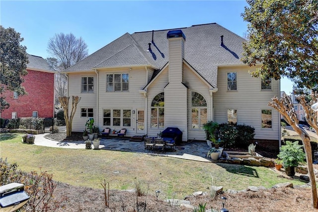 rear view of property with a shingled roof, a patio, a yard, and a chimney