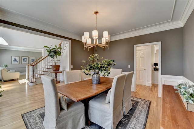 dining room with stairway, a notable chandelier, ornamental molding, and light wood finished floors