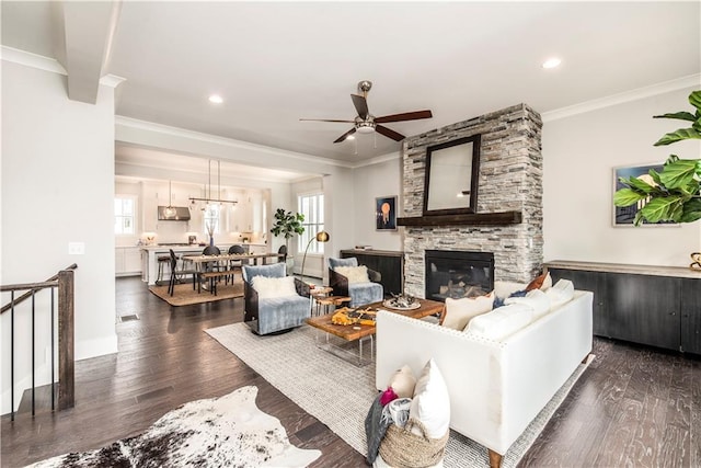 living room with ceiling fan, a fireplace, ornamental molding, and dark wood-type flooring