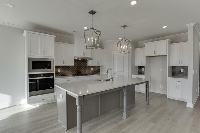 kitchen with a center island with sink, gas stovetop, built in microwave, oven, and white cabinetry