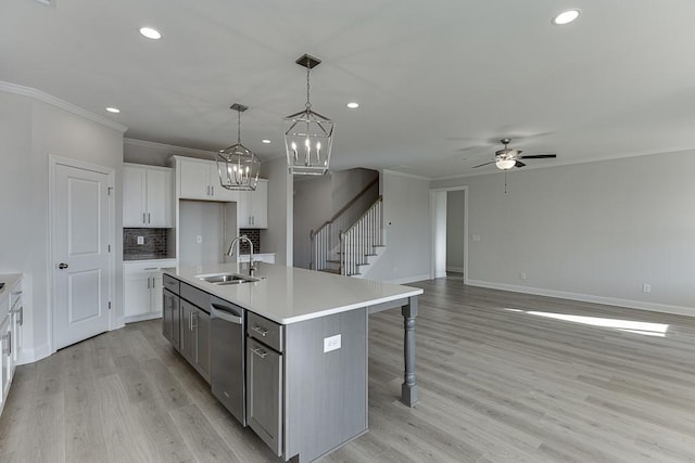 kitchen with stainless steel dishwasher, hanging light fixtures, an island with sink, white cabinetry, and sink