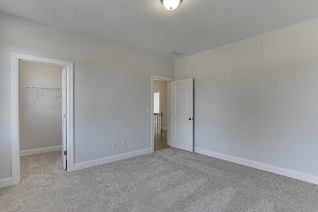 unfurnished bedroom with a walk in closet, a closet, and light carpet