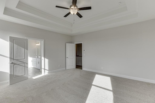 unfurnished bedroom with ensuite bathroom, ceiling fan, a tray ceiling, and light carpet