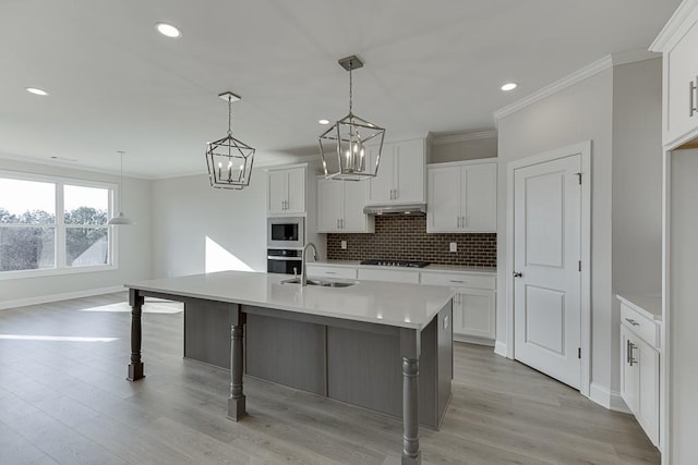 kitchen featuring stainless steel appliances, sink, decorative light fixtures, white cabinetry, and a center island with sink