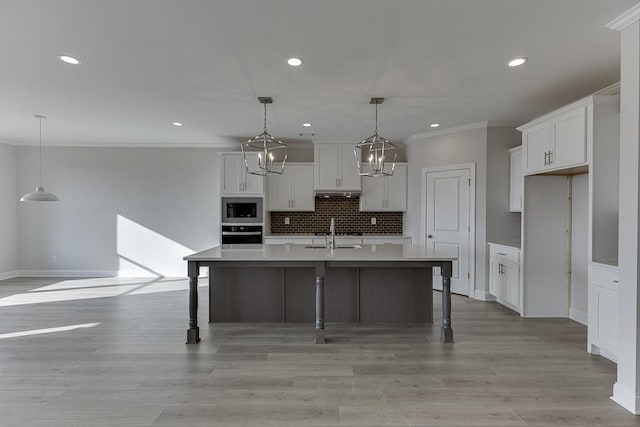 kitchen with sink, stainless steel oven, hanging light fixtures, a kitchen island with sink, and built in microwave