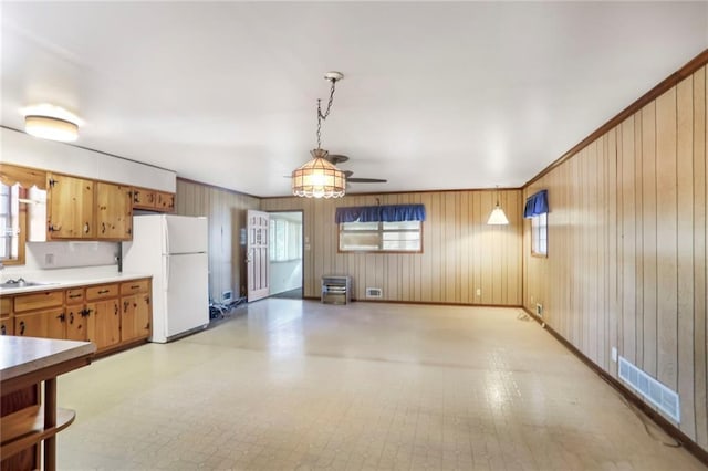 kitchen featuring visible vents, brown cabinets, freestanding refrigerator, hanging light fixtures, and light countertops