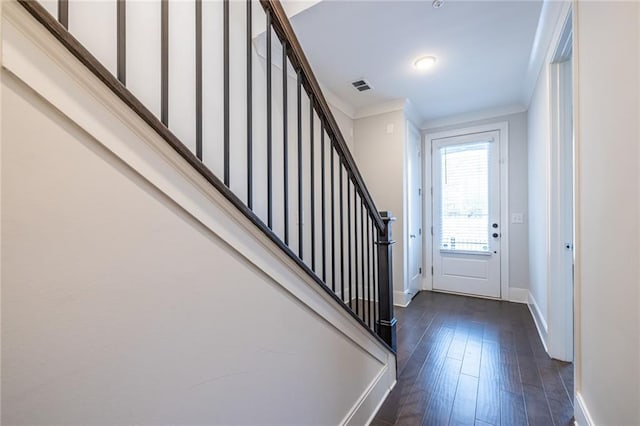 foyer entrance with dark wood-type flooring, visible vents, baseboards, stairs, and crown molding