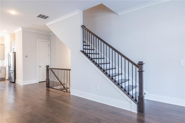 stairway with ornamental molding, wood finished floors, visible vents, and baseboards