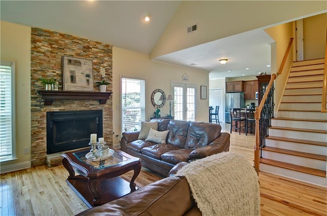 living room with light wood-type flooring, french doors, high vaulted ceiling, and a stone fireplace