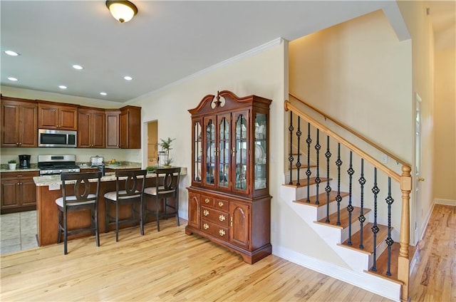 kitchen with light hardwood / wood-style floors, ornamental molding, stove, kitchen peninsula, and a breakfast bar