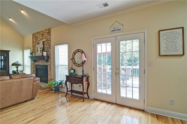 doorway to outside featuring light hardwood / wood-style flooring, a stone fireplace, french doors, crown molding, and lofted ceiling