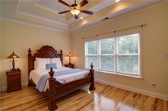 bedroom featuring light hardwood / wood-style floors, crown molding, ceiling fan, and a tray ceiling