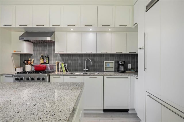 kitchen featuring wall chimney range hood, a sink, range, and white cabinets