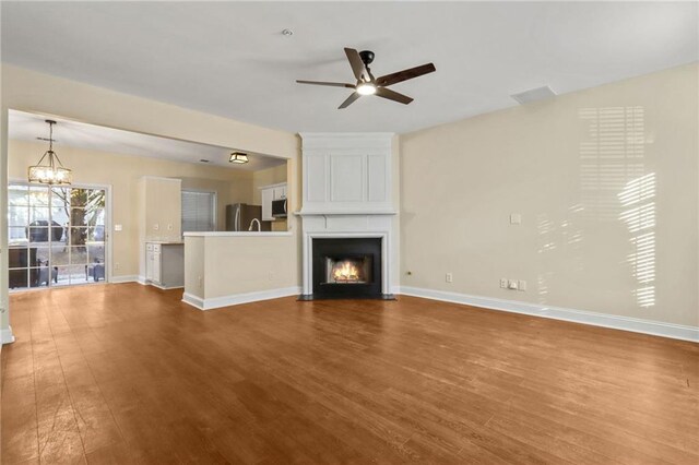 unfurnished living room with ceiling fan with notable chandelier, a large fireplace, and dark hardwood / wood-style floors