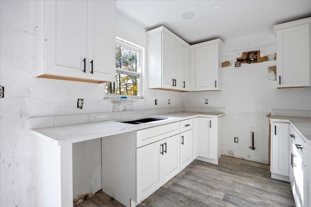 kitchen with light hardwood / wood-style flooring, white cabinets, light stone counters, and sink