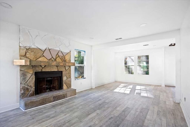 unfurnished living room with hardwood / wood-style floors and a stone fireplace