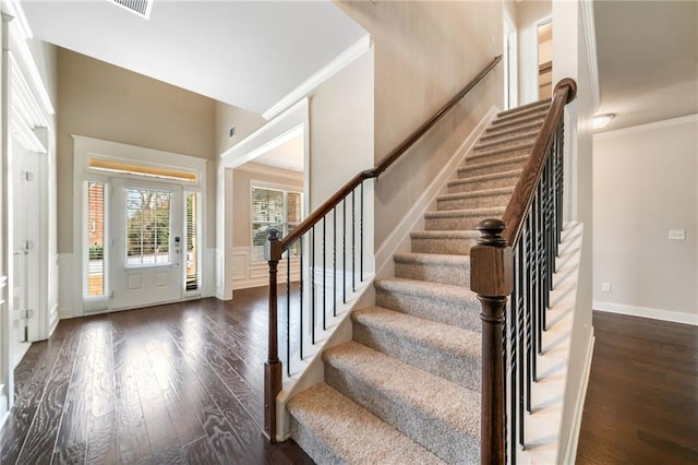 entrance foyer featuring a wainscoted wall, dark wood-type flooring, stairway, crown molding, and a decorative wall