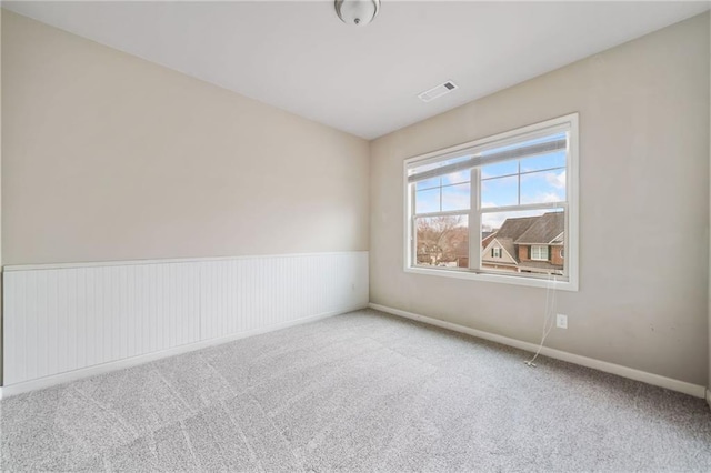 carpeted empty room with baseboards, visible vents, and wainscoting