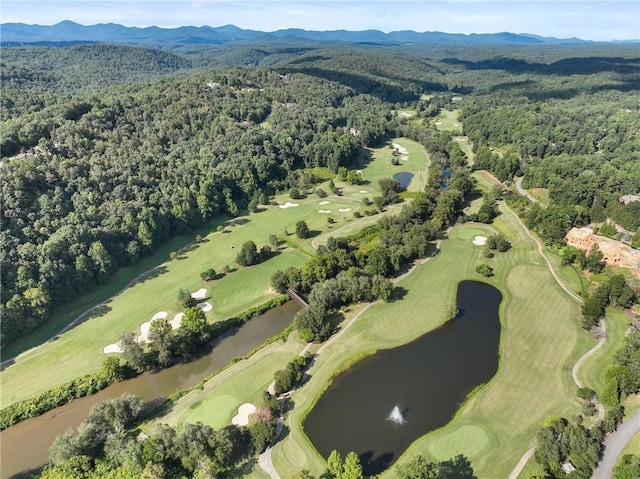 aerial view with a water and mountain view, view of golf course, and a forest view