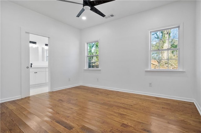 unfurnished bedroom featuring multiple windows, wood-type flooring, ensuite bathroom, and ceiling fan