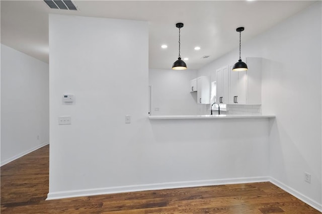 kitchen with white cabinets, dark hardwood / wood-style flooring, kitchen peninsula, and tasteful backsplash